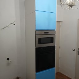 PIN - Wysoka zabudowa kuchenna z niebieskimi frontami i sprzętem AGD w Nysie. Widoczne niedokończone prace elektryczne i worki z zaprawą.