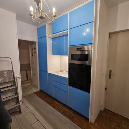 PIN - Niebieska zabudowa kuchenna z piekarnikiem i mikrofalówką, widok na fragment podłogi z dwoma rodzajami płytek, drabina malarska w rogu.