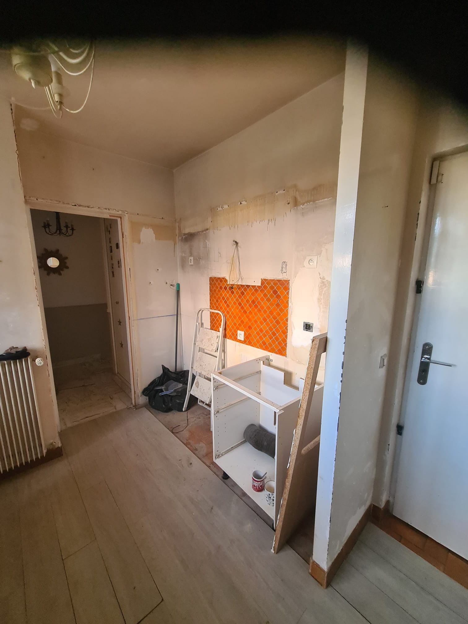 Wnętrze kuchni w trakcie remontu: częściowo zdemontowane szafki, odsłonięte fragmenty ścian z pomarańczowymi płytkami, drabina, widoczne ślady po instalacjach.