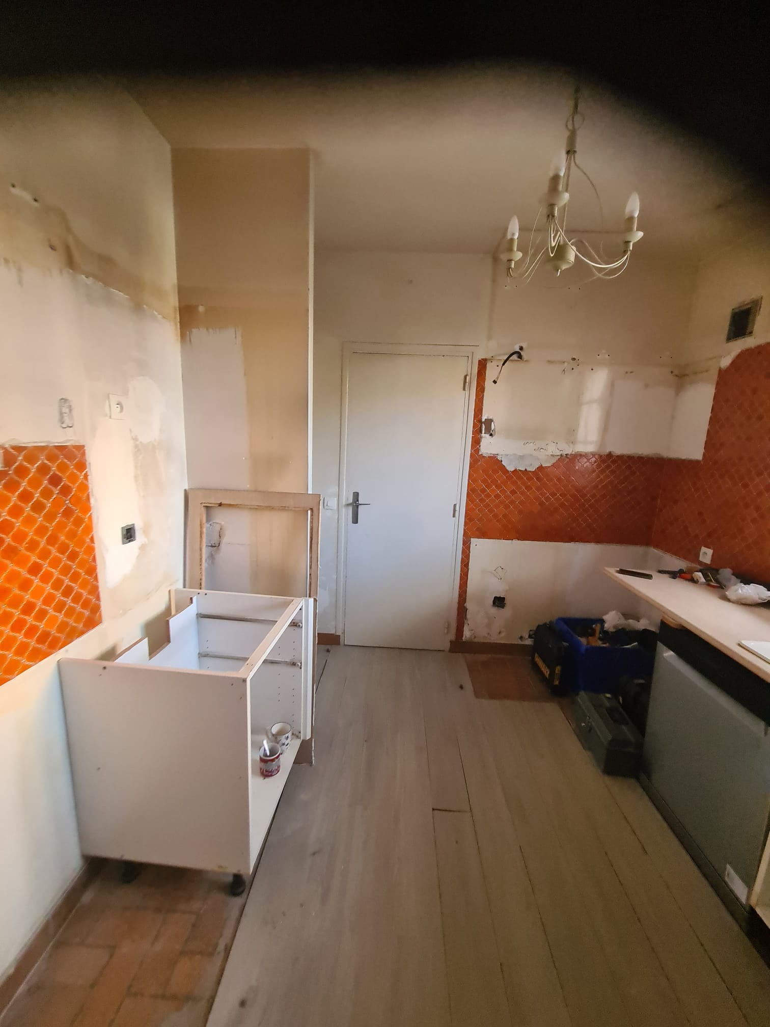 Wnętrze kuchni w trakcie remontu: częściowo zdemontowane szafki, odsłonięte fragmenty ścian z pomarańczowymi płytkami, narzędzia i skrzynki narzędziowe na podłodze.