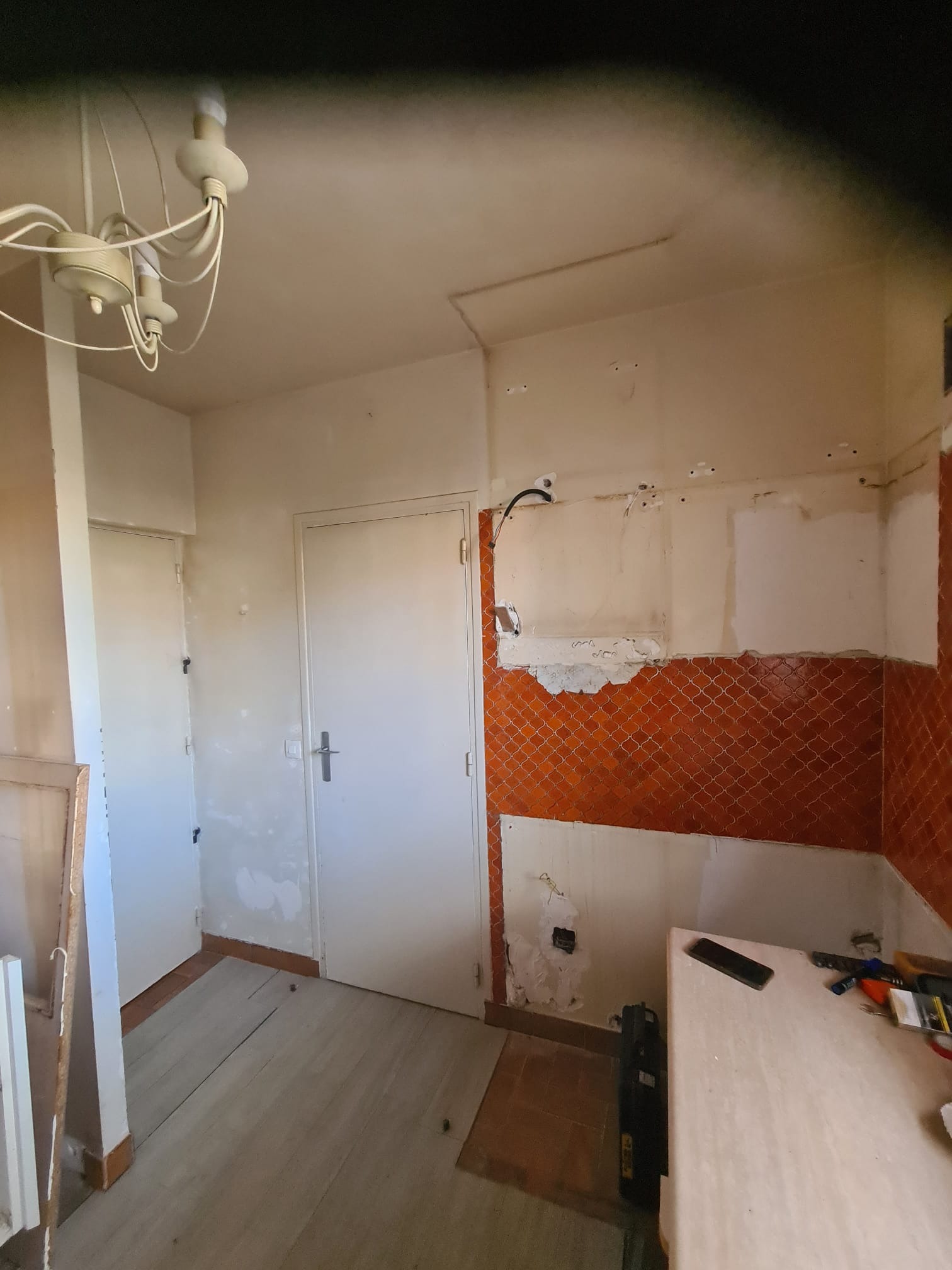 Remont kuchni w trakcie: częściowo zdjęte pomarańczowe płytki, odsłonięte przewody, widoczne narzędzia i fragmenty podłogi. Przygotowanie do dalszych prac wykończeniowych.