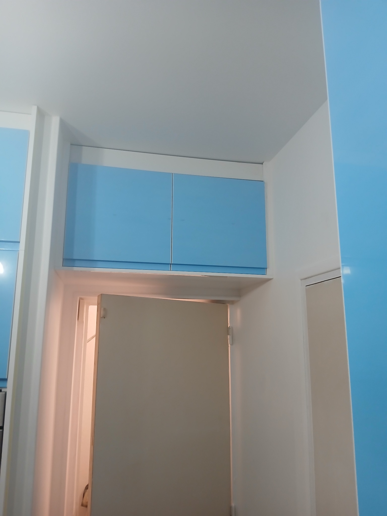 Niebieskie szafki nad otwartymi drzwiami w białej wnęce, widok z dołu. Minimalistyczny design, jasne kolory, nowoczesne wykończenie wnętrza.