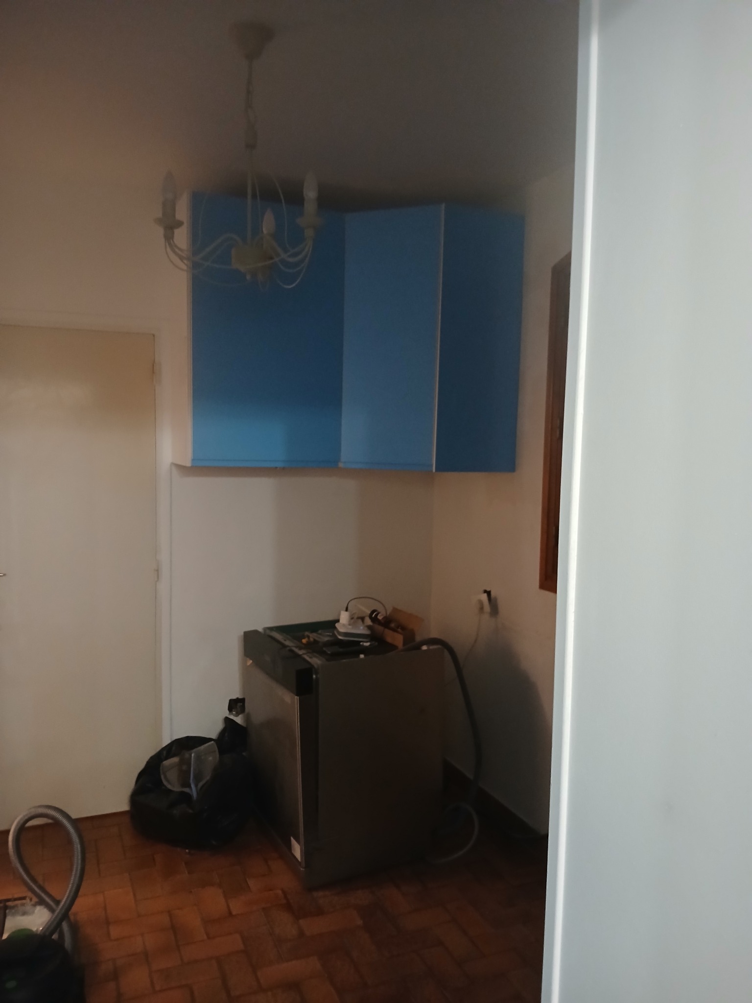 Narożna szafka kuchenna w kolorze niebieskim, zamontowana nad sprzętem AGD w trakcie prac wykończeniowych. Widoczna podłoga z parkietu i białe ściany.