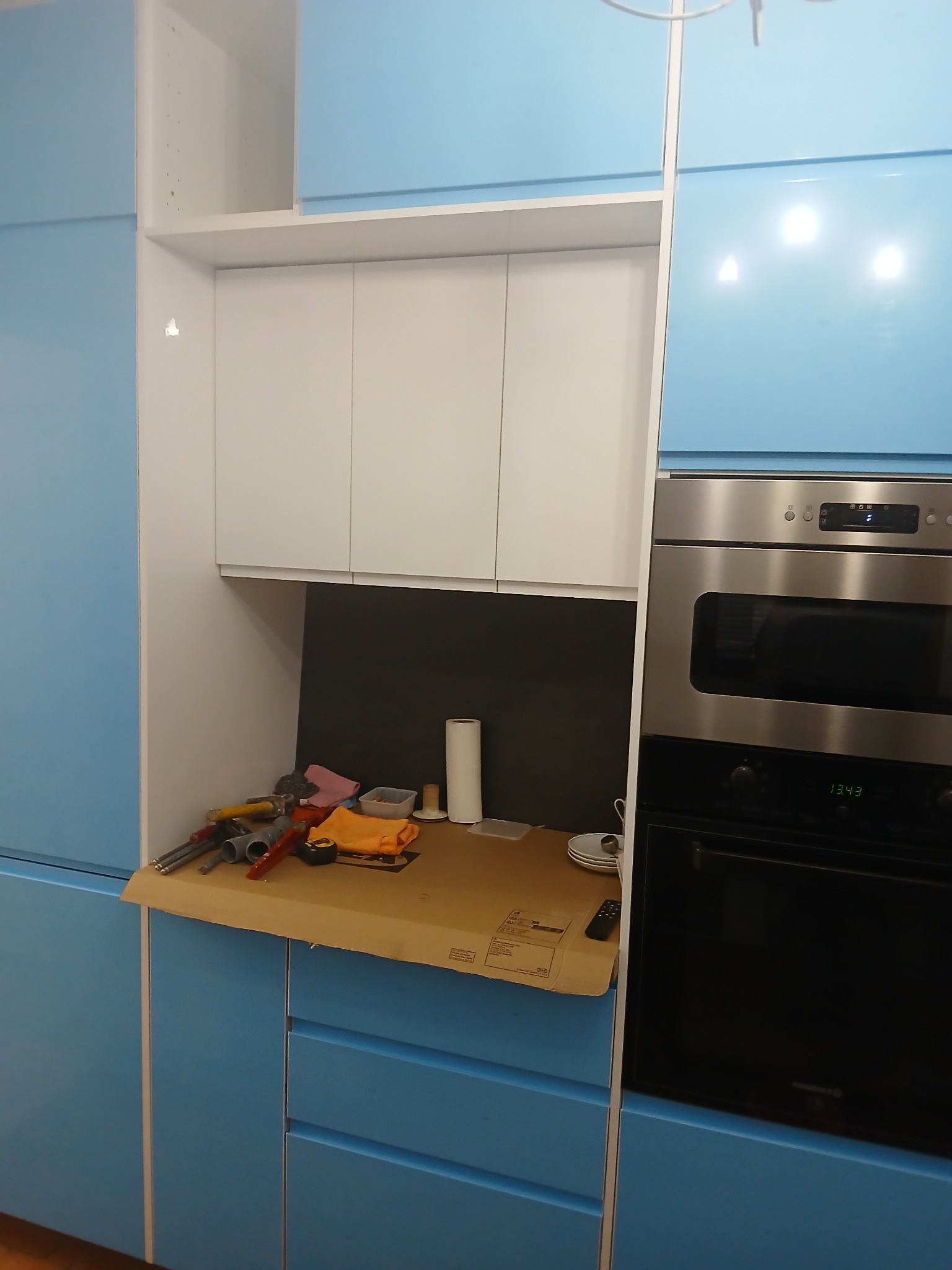 Niebiesko-biała zabudowa kuchenna w trakcie montażu. Na blacie roboczym narzędzia i akcesoria, obok piekarnik. Widoczne niedoskonałości montażu.