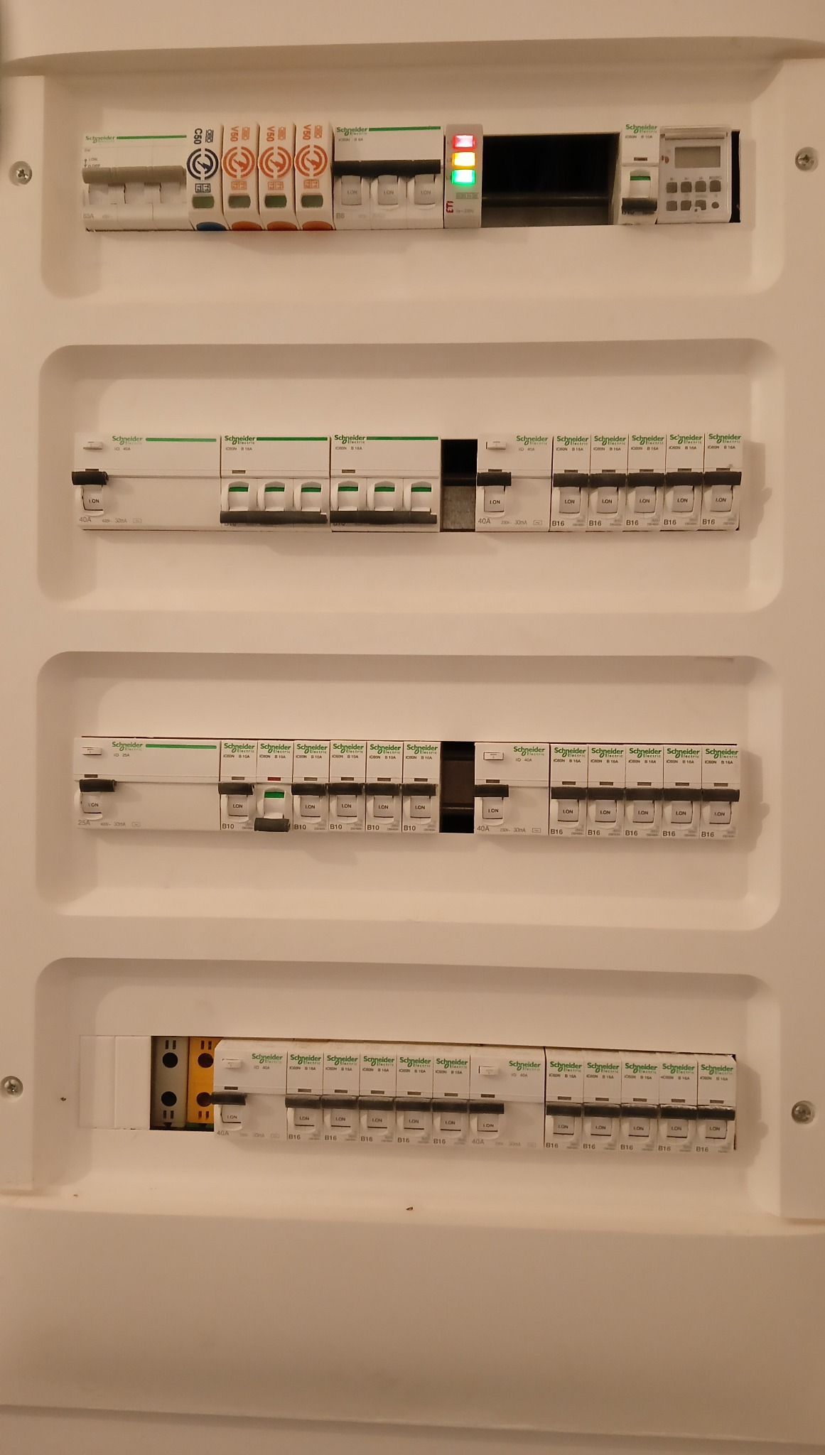 Rozdzielnica elektryczna z bezpiecznikami marki Schneider, widok z bliska. Elementy instalacji elektrycznej w białej obudowie. Bezpieczniki różnicowoprądowe i nadprądowe.