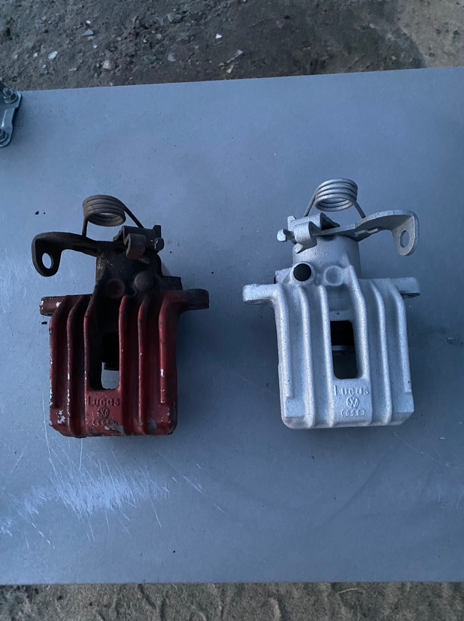 Dwa zaciski hamulcowe Lucas: stary, czerwony i nowy, srebrny, leżące obok siebie na szarym tle. Widoczny kontrast stanu przed i po renowacji.
