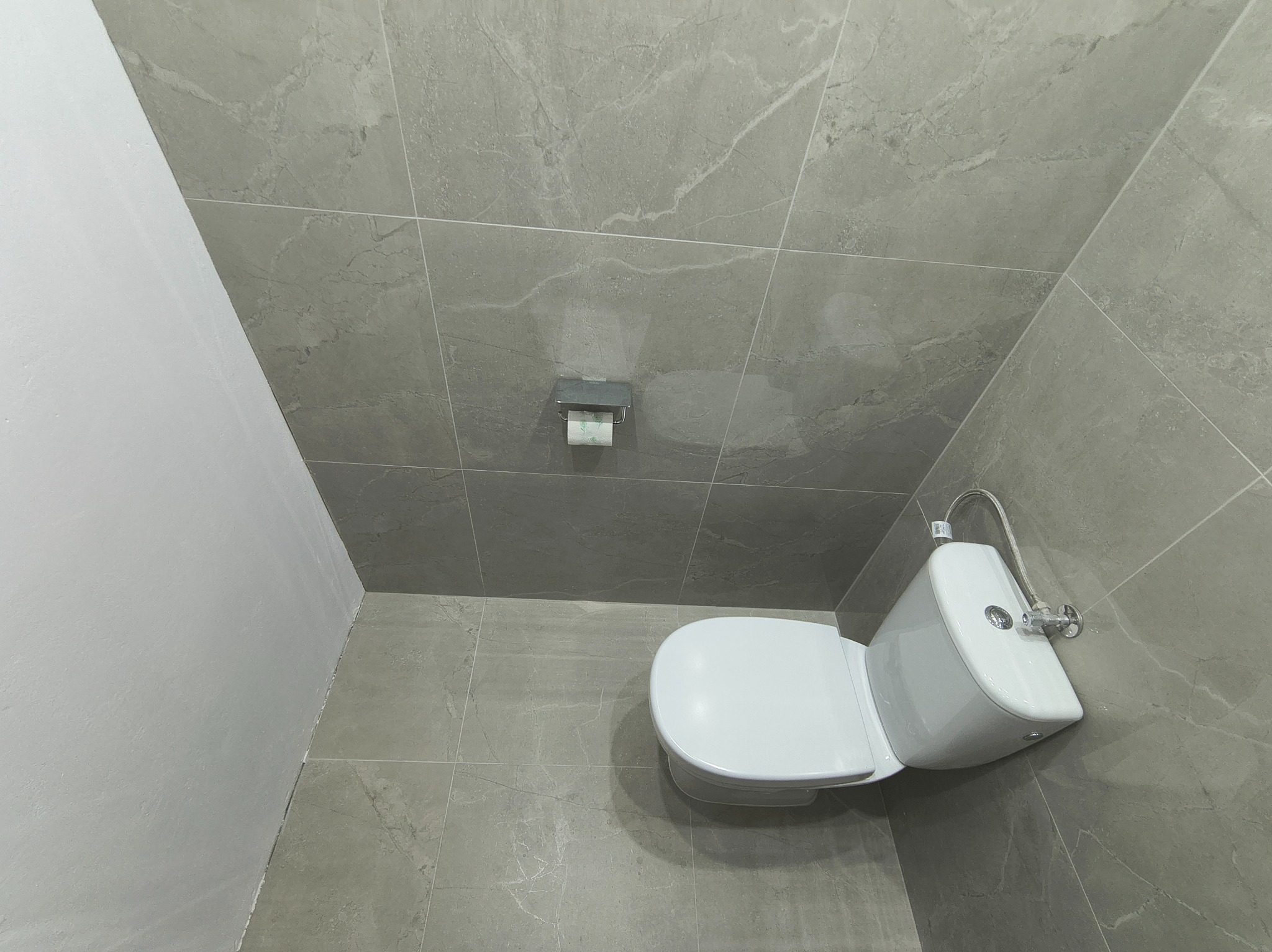 Wykończona łazienka z szarymi płytkami imitującymi marmur, białą toaletą i minimalistycznym uchwytem na papier toaletowy. Widok z góry, neutralne oświetlenie.