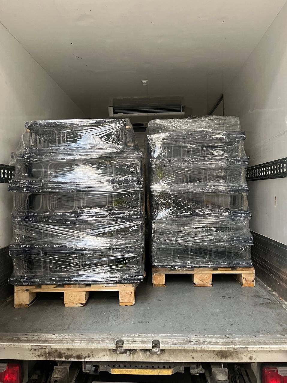 Dwie palety z czarnymi, owiniętymi folią ramami okiennymi wewnątrz przestrzeni ładunkowej samochodu dostawczego. Widoczne tylne światła pojazdu.