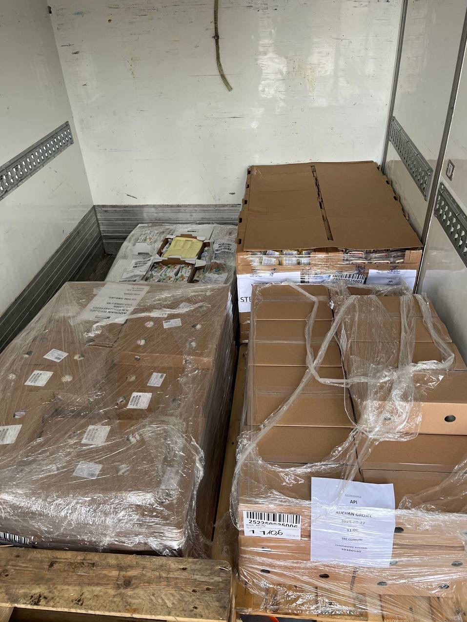 Kartonowe pudła z towarem, owinięte folią, ułożone wewnątrz przestrzeni ładunkowej pojazdu. Widoczne palety i etykiety z kodami kreskowymi.