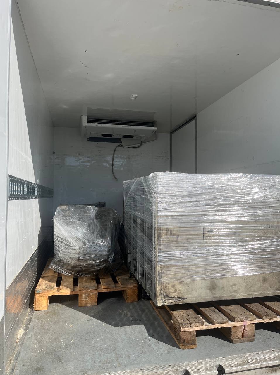 Wnętrze chłodni transportowej z dwoma ładunkami na paletach, zabezpieczonymi folią stretch. Widoczny agregat chłodniczy i szyny mocujące na ścianach.