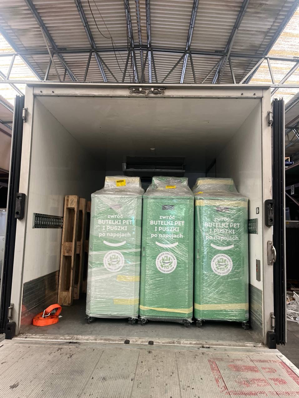 Załadunek pojemników na butelki PET i puszki w chłodni transportowej w Warszawie. Palety i pasy zabezpieczające ładunek. Usługi transportowe.