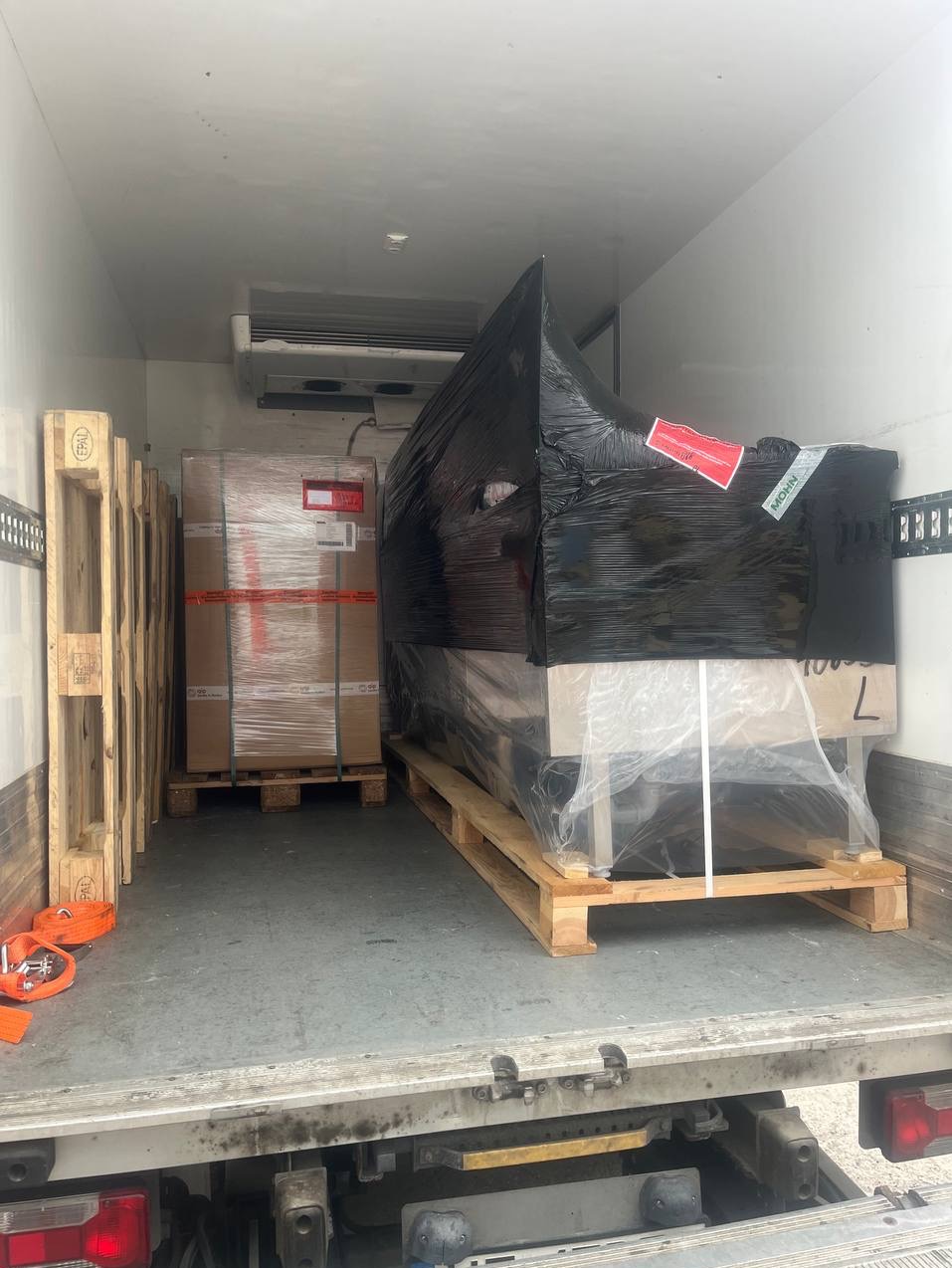 Wnętrze chłodni transportowej z paletami i zabezpieczonym ładunkiem: kartony oraz mebel owinięty folią i czarną folią stretch, gotowy do przewozu.