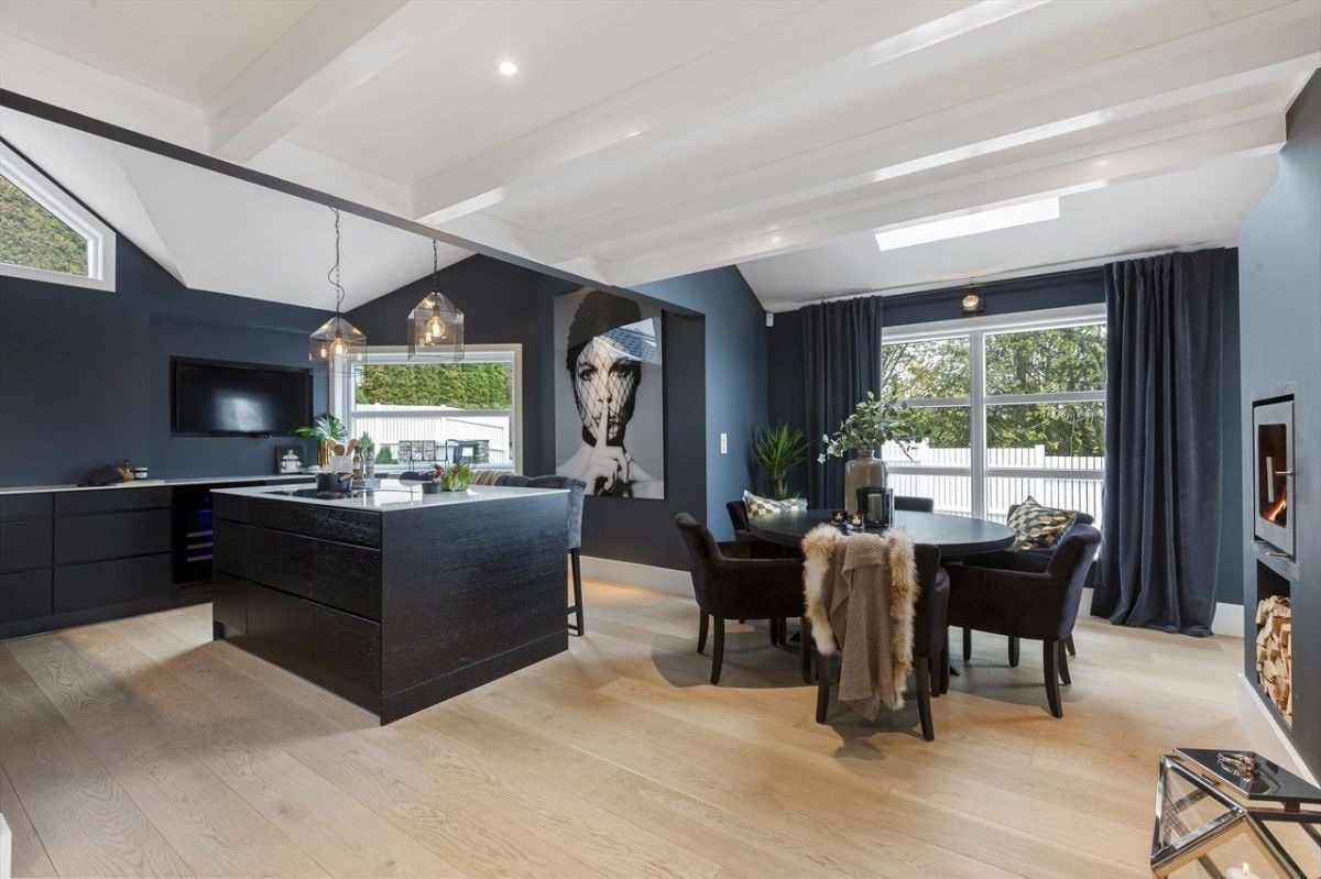 Eleganckie wnętrze: ciemne ściany, jasna podłoga, wyspa kuchenna, stół z krzesłami, grafika na ścianie i kominek. Nowoczesny design z dbałością o detale.