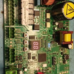 AK ENERGY Arkadiusz Krzywda - Płyta sterująca z elementami elektronicznymi, widoczne złącza, kondensatory, transformatory i wyświetlacz LED. Układ scalony na zielonym laminacie.