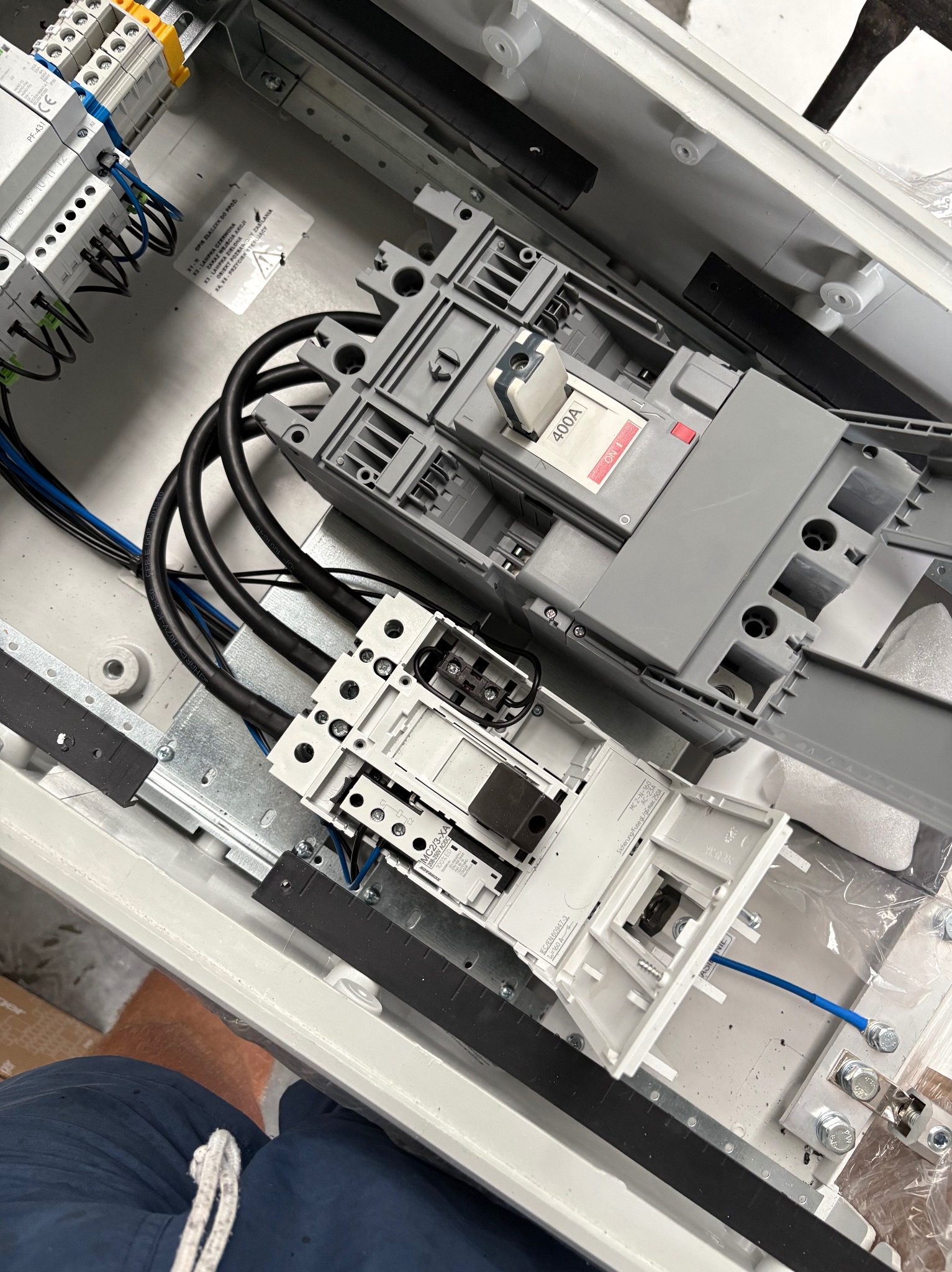 Rozdzielnica elektryczna w trakcie montażu, widoczne przewody, bezpieczniki i inne elementy instalacji. Detaliczne ujęcie wnętrza skrzynki z zamontowanymi komponentami.