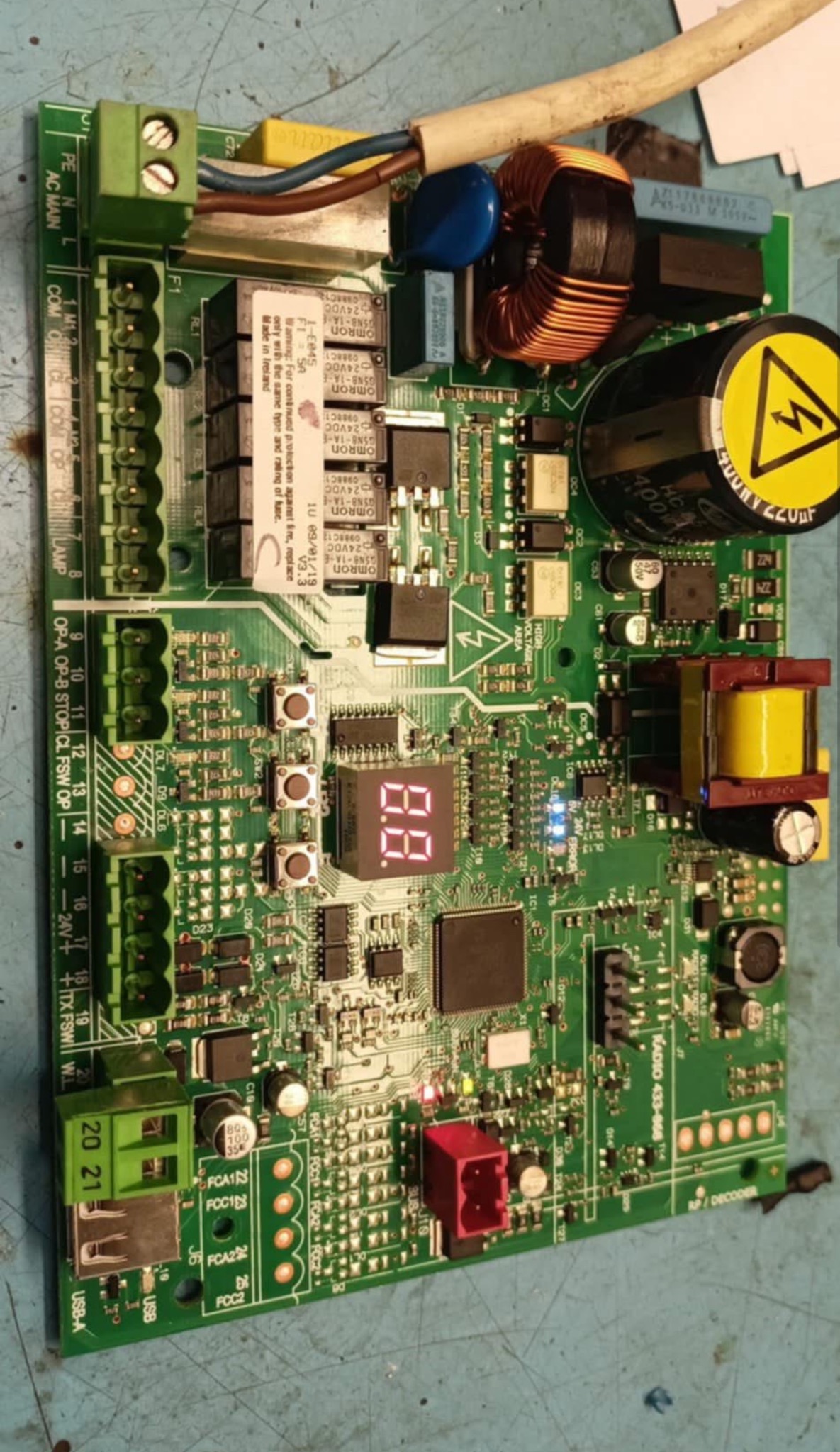 Płyta sterująca z elementami elektronicznymi, widoczne złącza, kondensatory, transformatory i wyświetlacz LED. Układ scalony na zielonym laminacie.