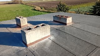 Szczegółowe ujęcie płaskiego dachu z trzema kominami w Mieszkowie. Widok z góry na pokrycie dachowe i elementy konstrukcyjne na tle zieleni.