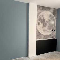 WRESTLING Bohdan Varshavskyi - Niebieska ściana, biała kolumna i fototapeta z motywem księżyca w pokoju po remoncie, z widocznymi zabezpieczeniami podłogi.