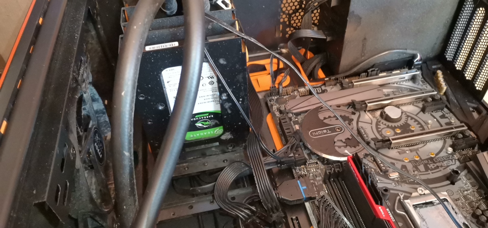 Wnętrze brudnej obudowy komputera stacjonarnego z widoczną płytą główną ASRock Z390 Taichi, dyskiem twardym Seagate Barracuda i elementami chłodzenia wodnego.