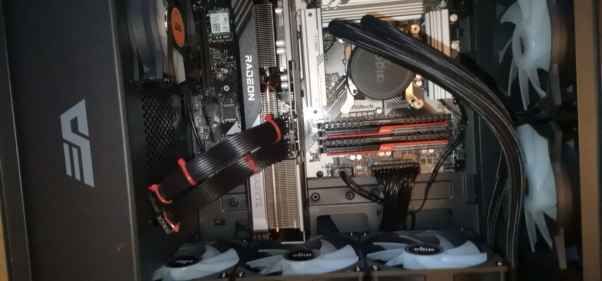 Wnętrze komputera stacjonarnego z kartą graficzną Radeon, chłodzeniem wodnym Aigo i płytą główną ASRock B760 Pro RS/D4. Widoczne wentylatory i pamięć RAM Corsair.