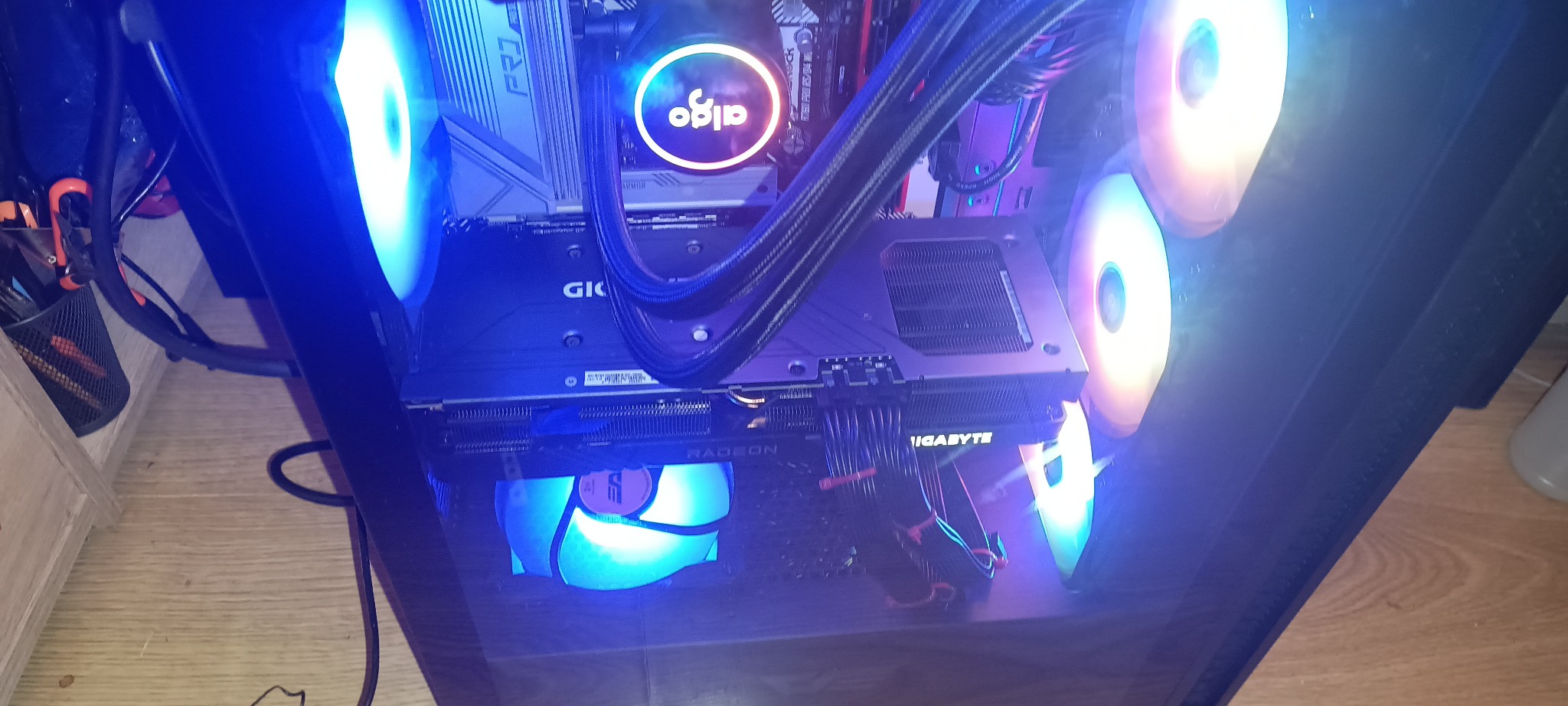 Wnętrze gamingowego PC z podświetleniem RGB: karta graficzna Gigabyte Radeon, chłodzenie wodne Aigo, wentylatory. Widok z góry na komponenty w obudowie.