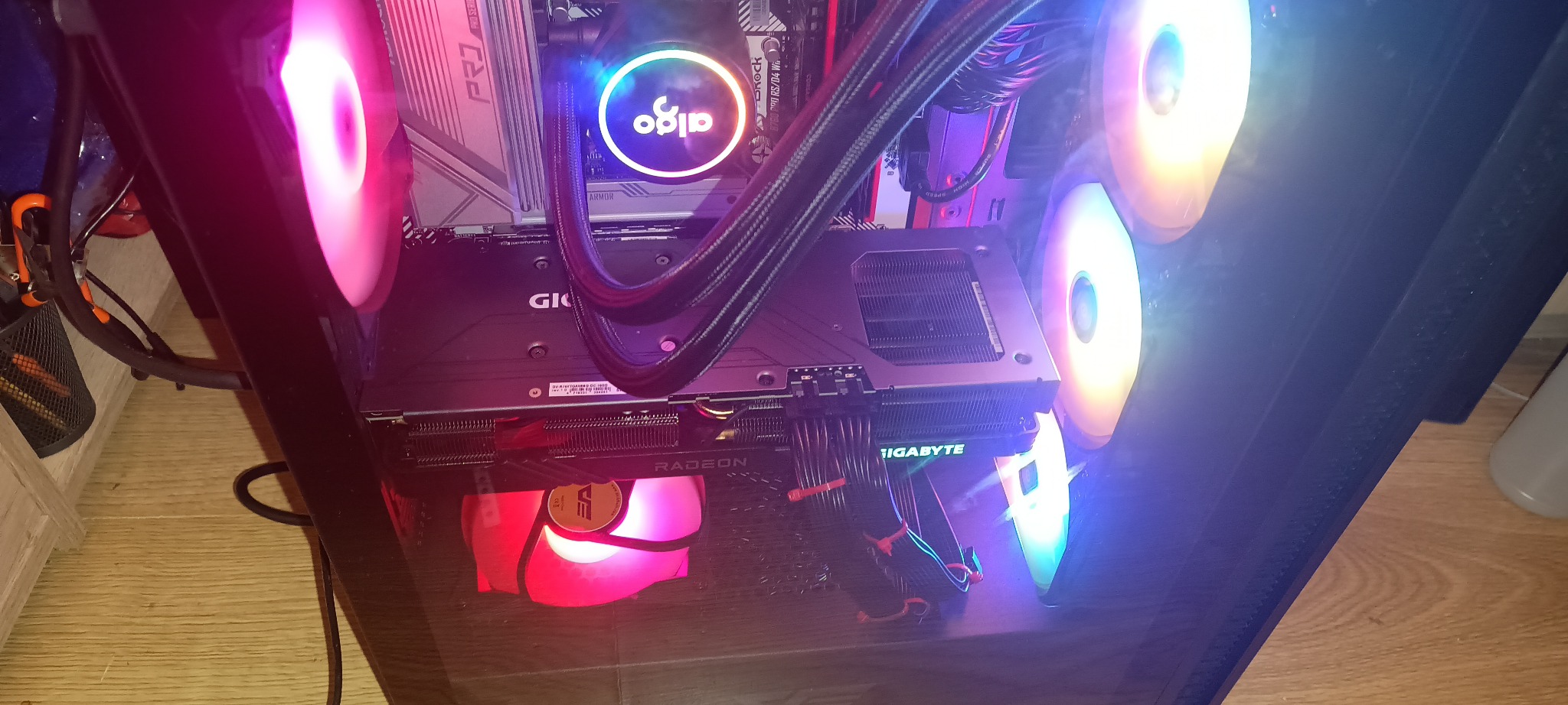 Wnętrze komputera stacjonarnego z podświetleniem RGB: karta graficzna Radeon Gigabyte, chłodzenie wodne Aigo i wentylatory. Widok z góry na komponenty PC.