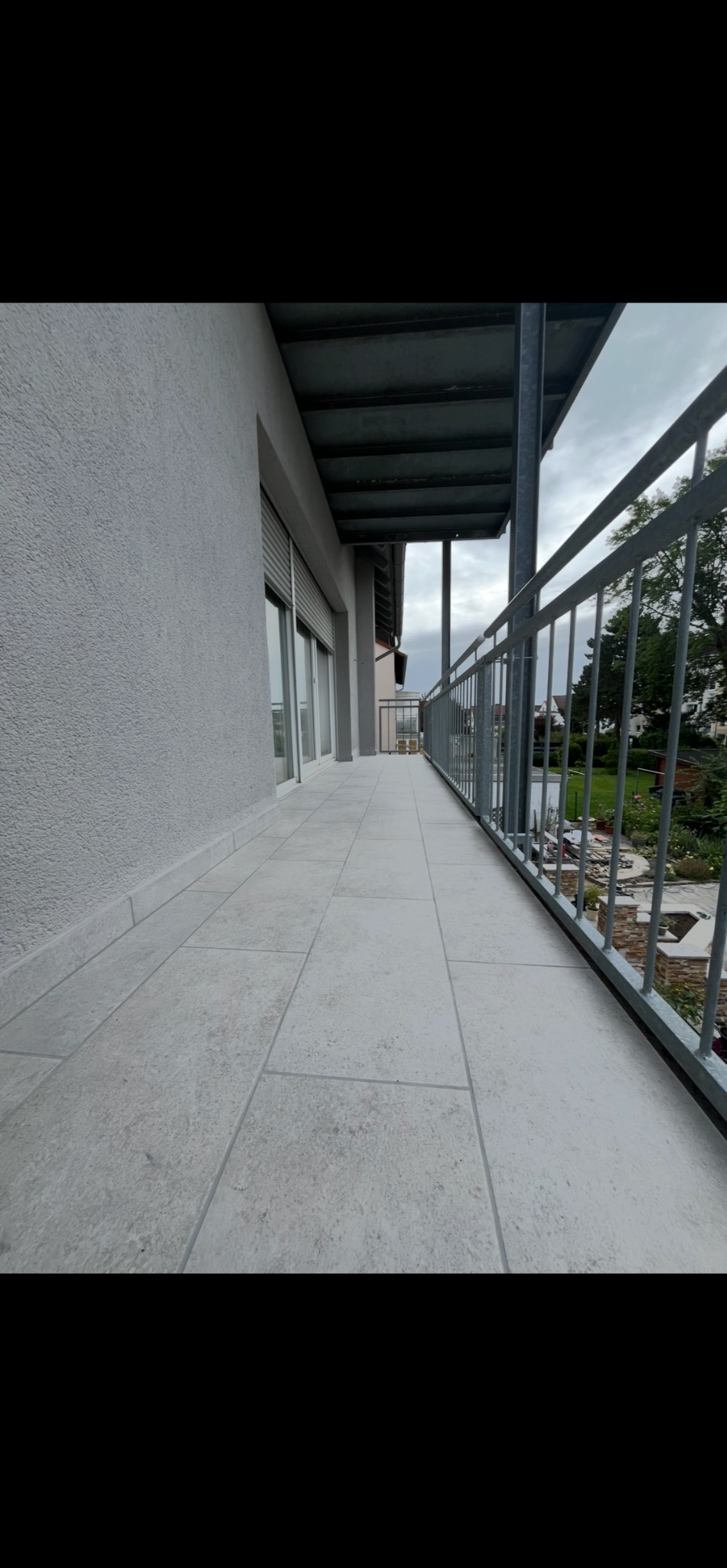 Jasne, kwadratowe płytki na balkonie z metalową balustradą. Widok na zewnątrz, szare niebo. Minimalistyczny design, czyste linie, nowoczesne wykończenie.