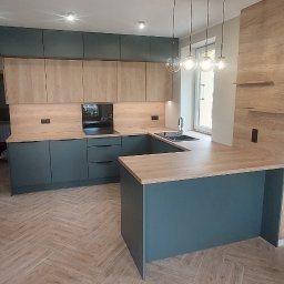 Baker Meble - Nowoczesna kuchnia z wyspą, fronty w kolorze butelkowej zieleni i drewnopodobne blaty. Parkiet ułożony w jodełkę. Nad wyspą wiszą cztery szklane lampy.