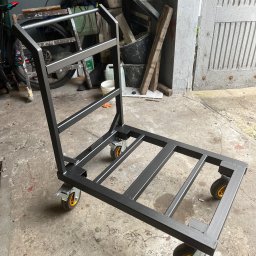 Mobilne Usługi Spawalnicze - Wózek transportowy ze stali, spawany, malowany proszkowo na czarno, z czterema kołami. Wykonany przez ślusarza z Częstochowy. Widoczne spawy i elementy konstrukcyjne.