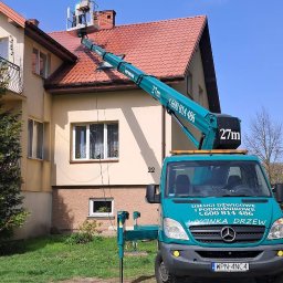 Mycie dachu z podnośnika koszowego. Czerwona dachówka, beżowa elewacja budynku. Na podnośniku osoba w kasku. Usługi dźwigowe i wycinka drzew.