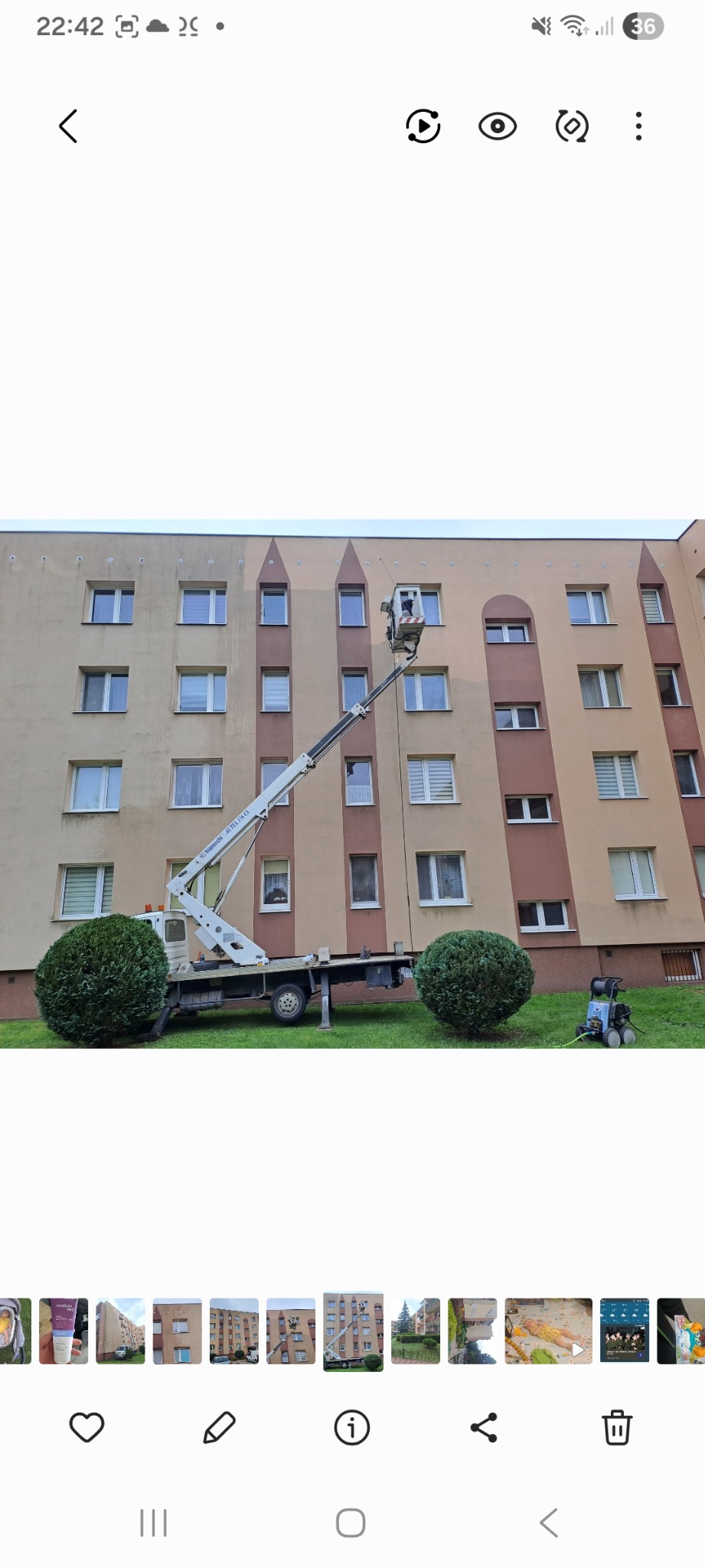 Praca na wysokościach: podnośnik koszowy przy bloku, pracownik w koszu. Częściowo umyta elewacja w odcieniach beżu i brązu. Widoczna myjka ciśnieniowa na trawniku.