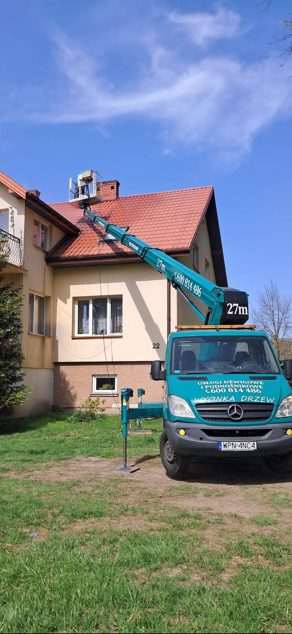 Mycie dachu z podnośnika koszowego. Czerwona dachówka, beżowa elewacja budynku. Na podnośniku osoba w kasku. Usługi dźwigowe i wycinka drzew.