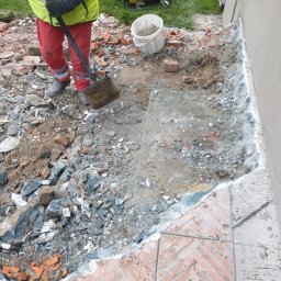 FENIX JAROSŁAW OLSZOWSKI GardenFenix Magdalena Michnik - Przygotowanie wykopu pod fundament w Bielsko-Białej. Fragment muru, gruz, ziemia, narzędzia. Prace ziemne w toku, widoczny agregat prądotwórczy.