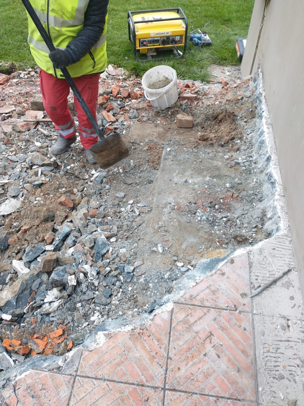 Przygotowanie wykopu pod fundament w Bielsko-Białej. Fragment muru, gruz, ziemia, narzędzia. Prace ziemne w toku, widoczny agregat prądotwórczy.