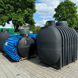 FOL-KUL SPÓŁKA Z OGRANICZONĄ ODPOWIEDZIALNOŚCIĄ - Czarne zbiorniki na paletach i niebieskie rury na zewnątrz, w tle drzewa i błękitne niebo. Elementy systemów odwodnień i oczyszczalni.