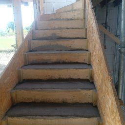 Waldi Bau - Surowe schody betonowe w drewnianym szalunku na budowie, widoczne podpory i bloczki. Etap wylewania stopni, surowy stan, widok z dołu.