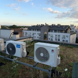 BRIMAN SPÓŁKA Z OGRANICZONĄ ODPOWIEDZIALNOŚCIĄ - Trzy zewnętrzne jednostki klimatyzacji LG, Midea i GREE zamontowane na metalowej konstrukcji na zielonym dachu, z widokiem na miejską zabudowę.