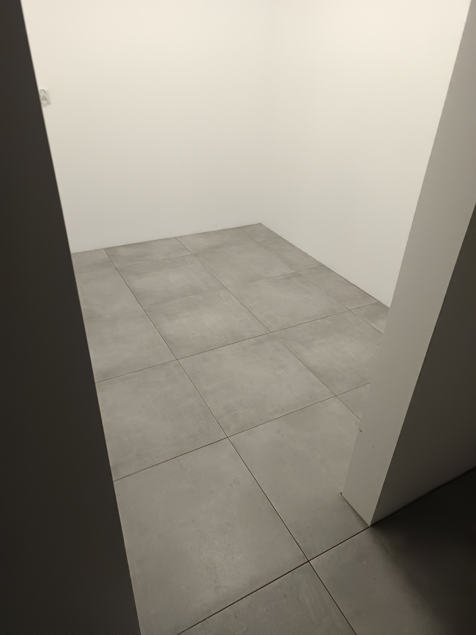Wykończone wnętrze z szarymi płytkami podłogowymi i białymi ścianami, widoczne z perspektywy wejścia. Minimalistyczny design, neutralna kolorystyka.