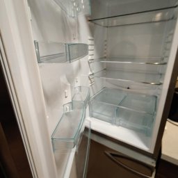 Homedetailingswarzedz - Pusta lodówka z przezroczystymi półkami i szufladami, widok z boku, wnętrze oświetlone, gotowa do napełnienia produktami spożywczymi.