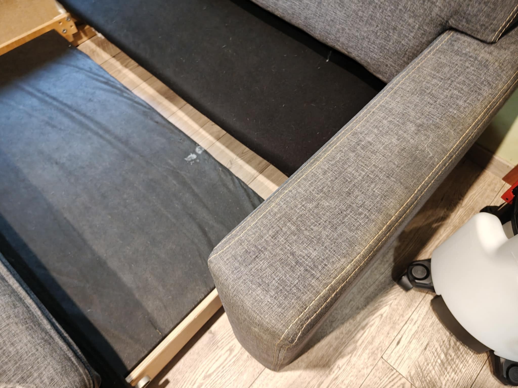 Szara kanapa z wysuwanym siedziskiem, widoczna struktura materiału i drewniany stelaż. Usługa w Swarzędzu.