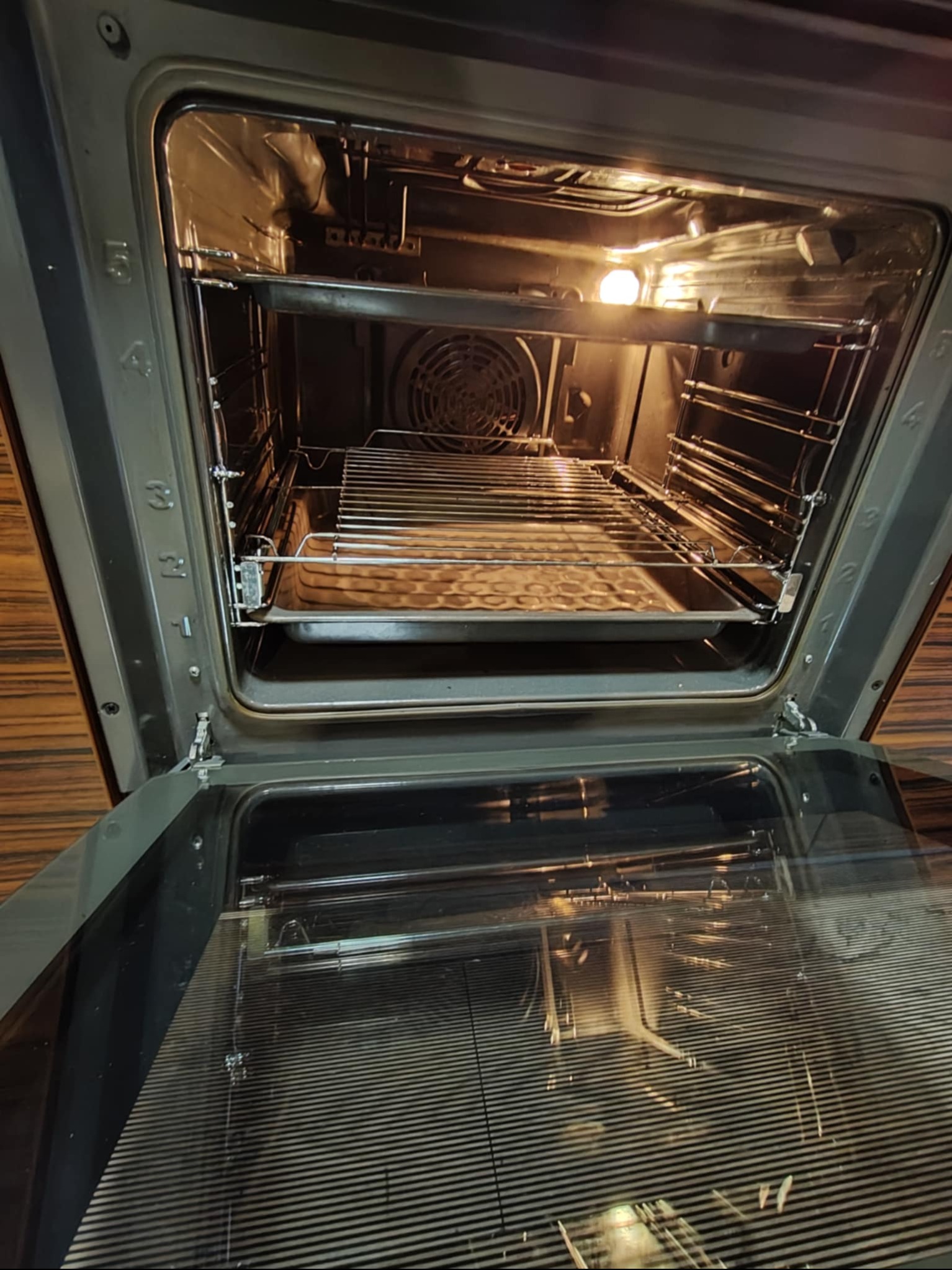 Otwarty piekarnik z widoczną kratką i blachą wewnątrz, oświetlony od środka. Widoczne ślady użytkowania na ściankach piekarnika.