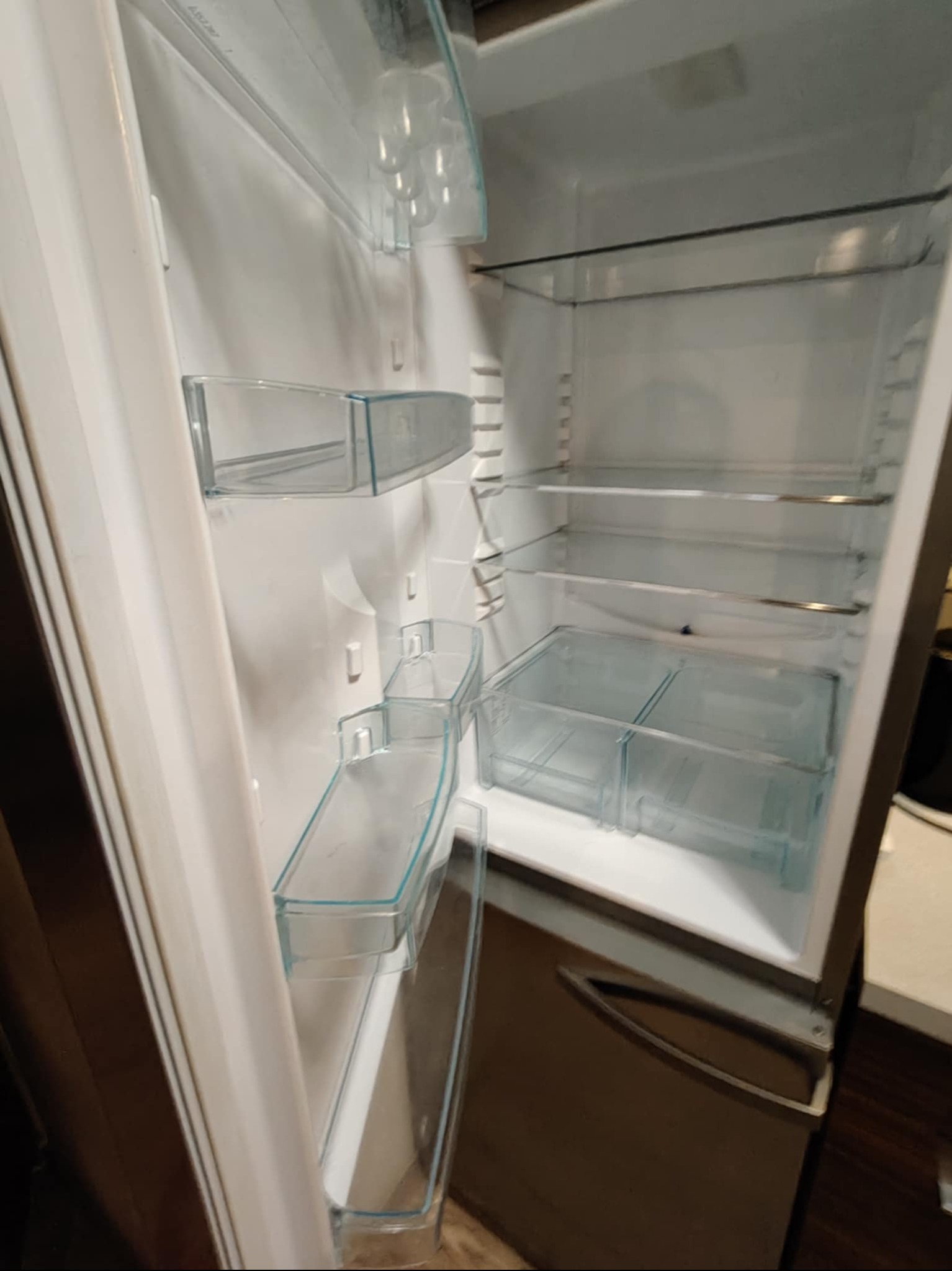 Pusta lodówka z przezroczystymi półkami i szufladami, widok z boku, wnętrze oświetlone, gotowa do napełnienia produktami spożywczymi.