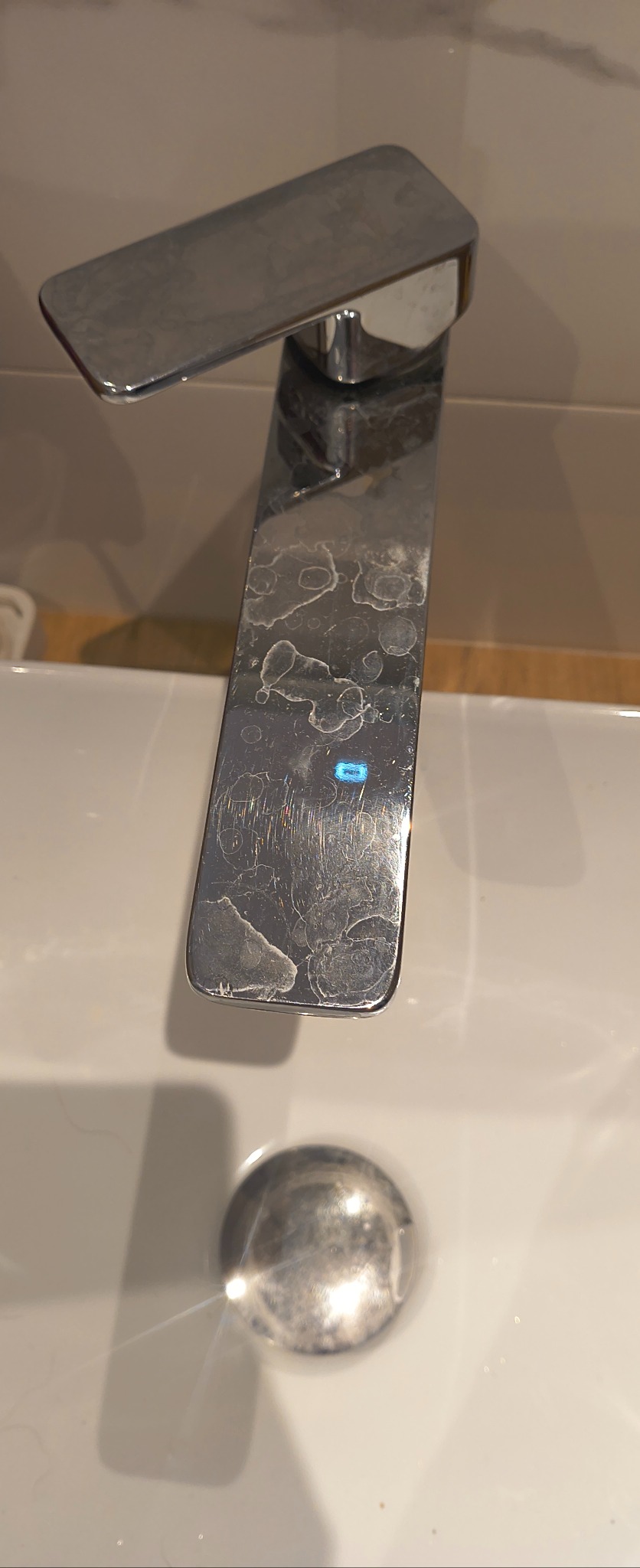 Bateria umywalkowa ze śladami po twardej wodzie i osadami, widoczne zacieki na chromowanej powierzchni. Ujęcie z góry, skupione na detalu.