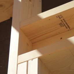 BUDUJE-GRUPA Spółka z ograniczoną odpowiedzialnością - Fragment konstrukcji domu szkieletowego z jasnego drewna, widoczne połączenia elementów, oznaczenia na drewnie. Ujęcie z bliska, ostre światło.