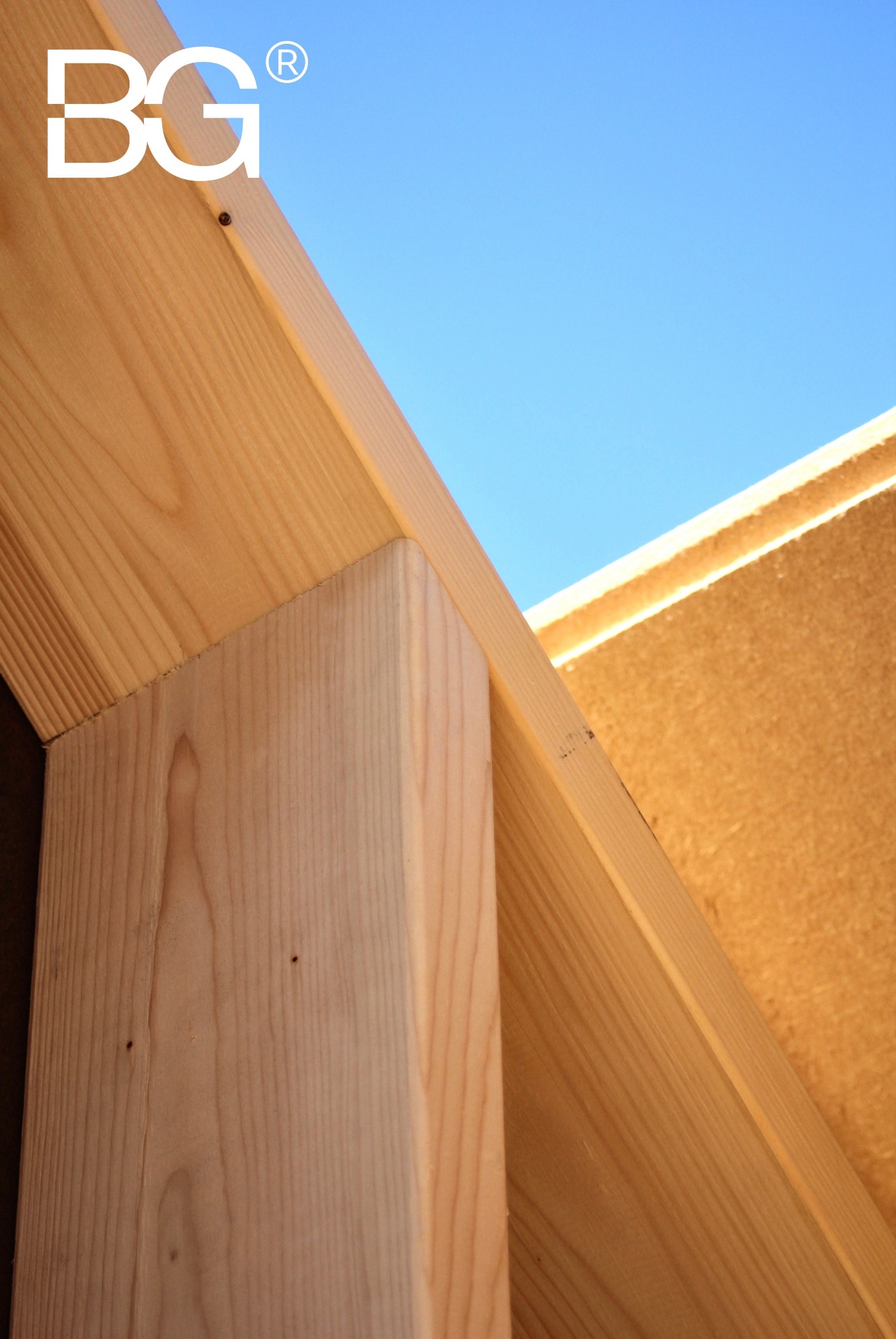 Fragment konstrukcji drewnianej domu w budowie, widok z dołu na jasne drewno i błękitne niebo. Widoczny słup, belka i poszycie. Logo w lewym górnym rogu.