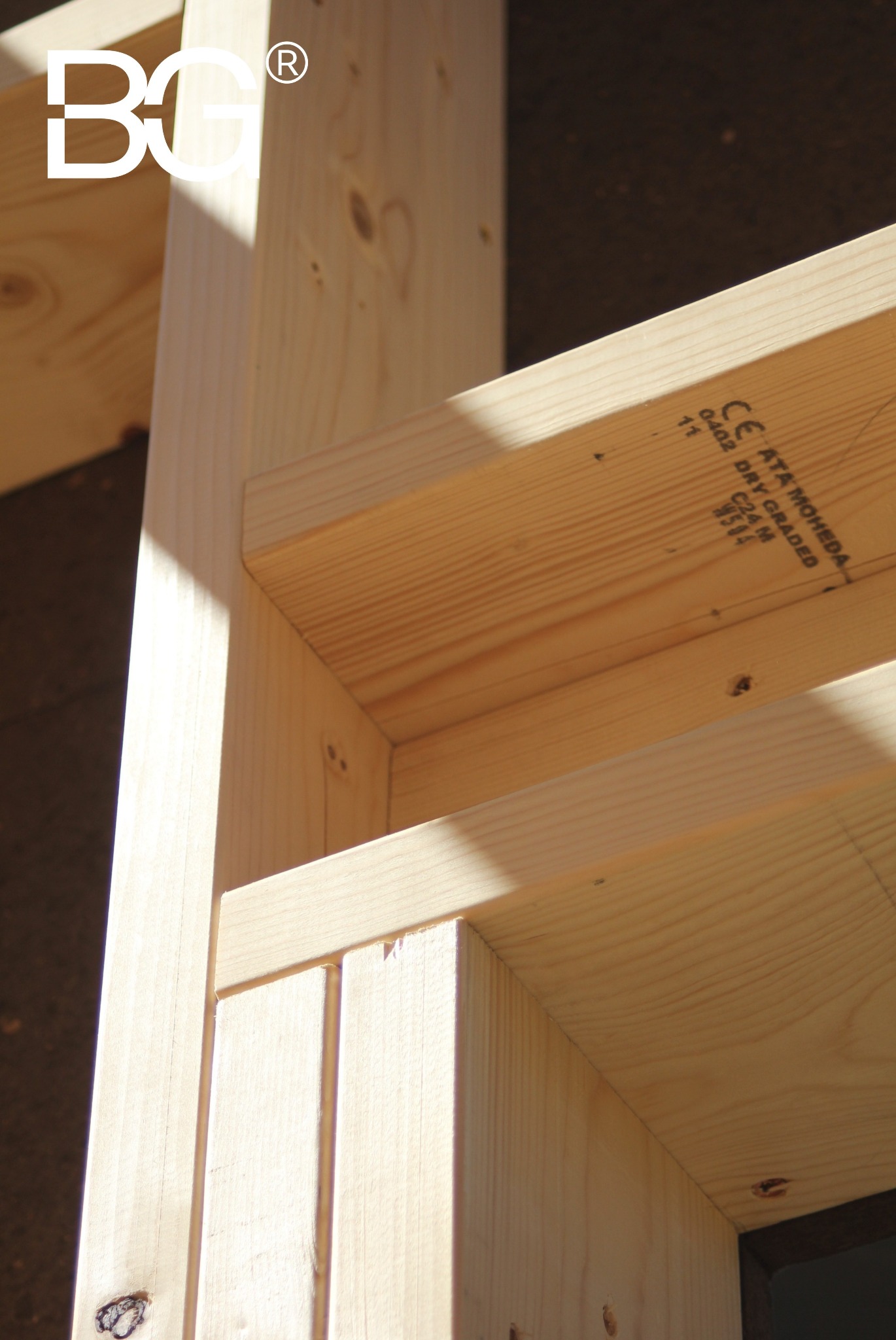 Fragment konstrukcji domu szkieletowego z jasnego drewna, widoczne połączenia elementów, oznaczenia na drewnie. Ujęcie z bliska, ostre światło.