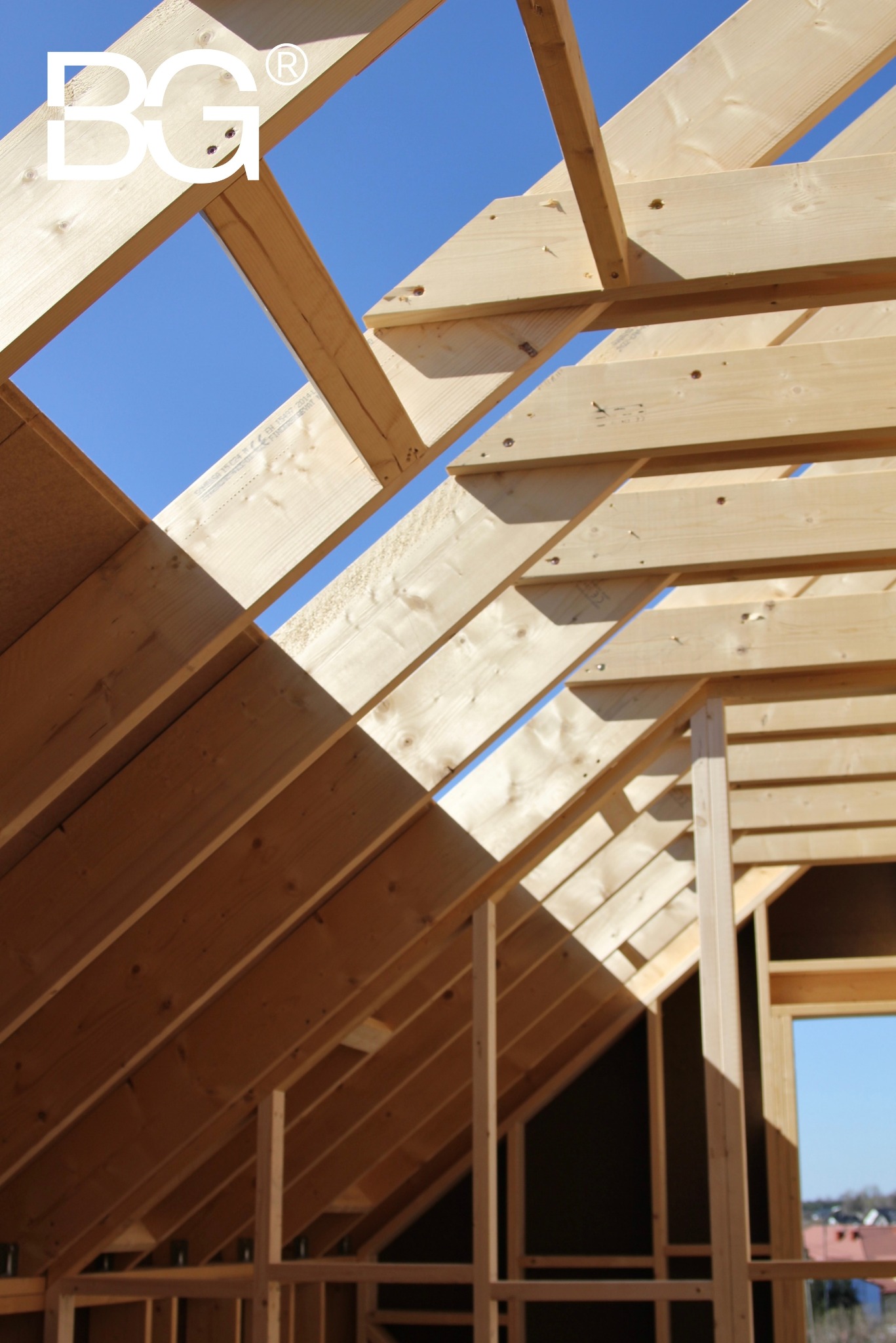 Konstrukcja drewniana dachu w trakcie budowy, widok z dołu na jasne belki i fragment błękitnego nieba. Elementy złączone śrubami, widoczne detale drewna.