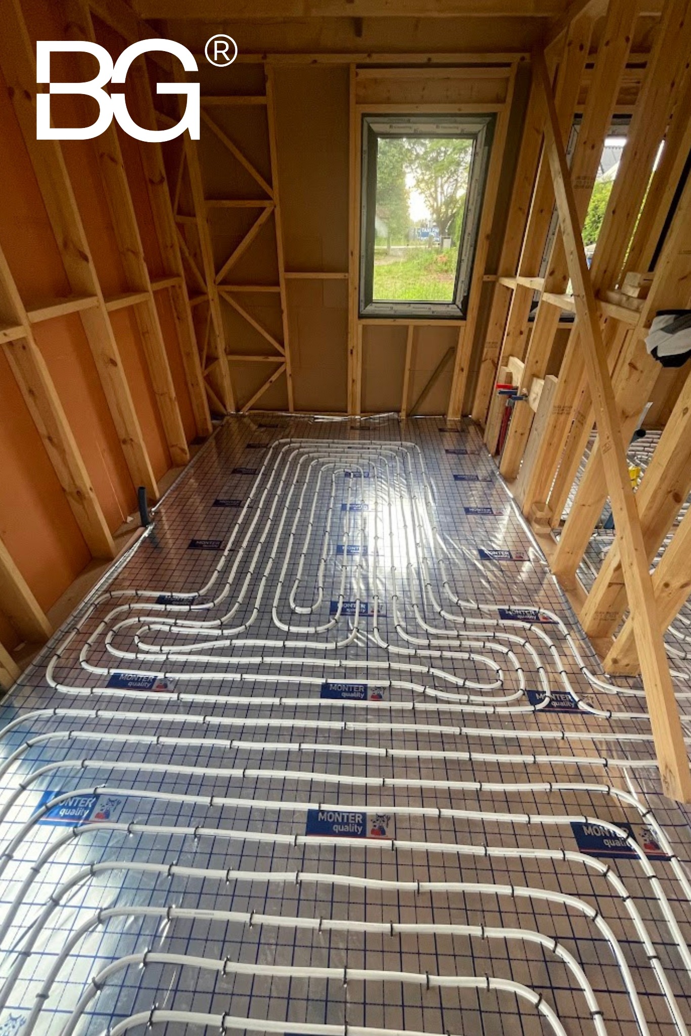 Instalacja ogrzewania podłogowego w domu szkieletowym, rury ułożone na folii z siatką, widoczne drewniane elementy konstrukcji dachu i okno dachowe.