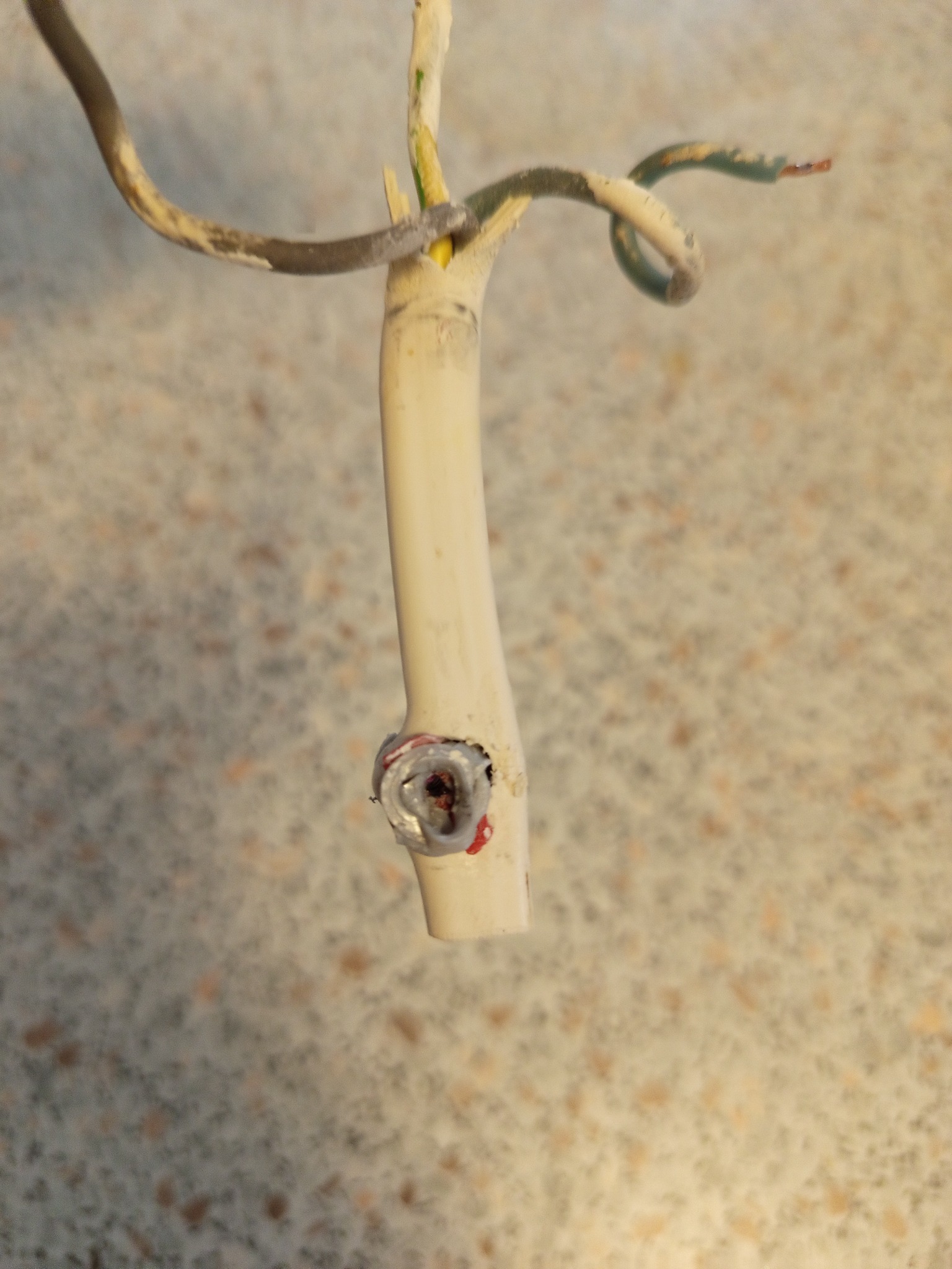 Uszkodzony kabel elektryczny wystający ze ściany, z widocznymi przewodami i śladami po naprawie. Niefortunny widok po demontażu lampy.