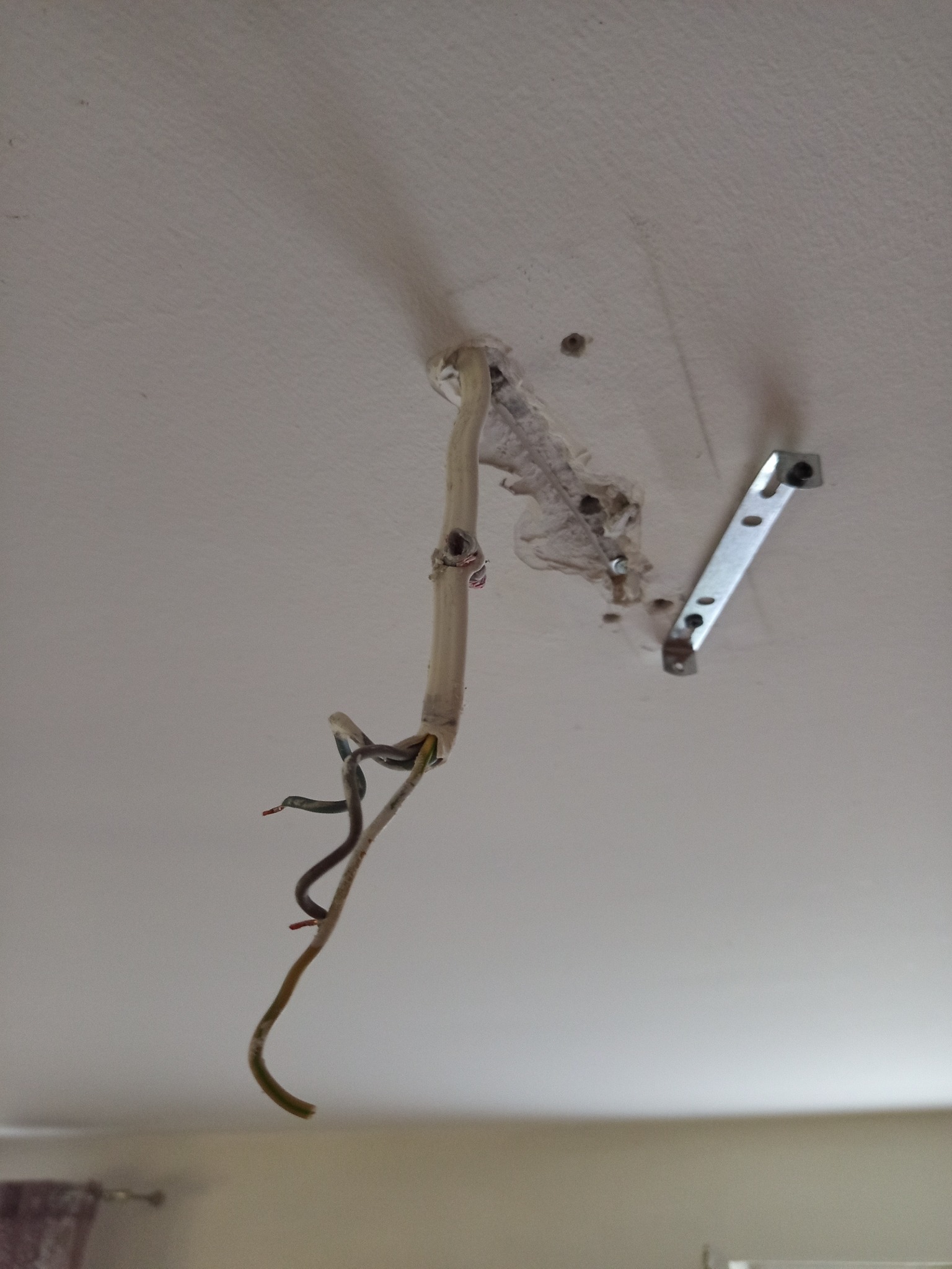 Odsłonięte przewody elektryczne wystające z sufitu obok metalowego uchwytu montażowego, przygotowane do instalacji oświetlenia.